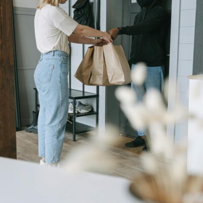 A woman receives a delivery package from a courier at her doorstep inside a modern home.