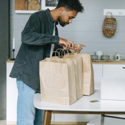 Young man organizing paper shopping bags indoors in a modern kitchen setting.